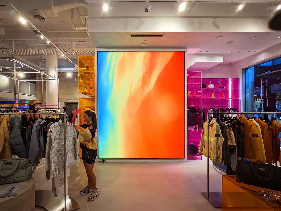 Vertical LED display inside P.E Nation retail store showing abstract colourful visuals among clothing racks.