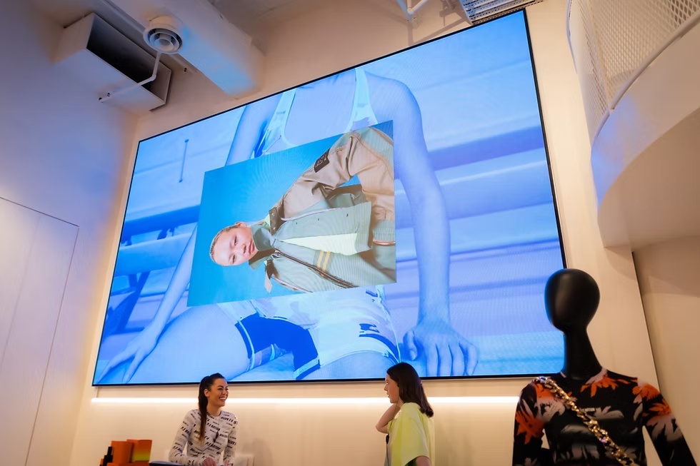 P.E Nation retail store with large LED display showing fashion campaign visuals above shoppers.